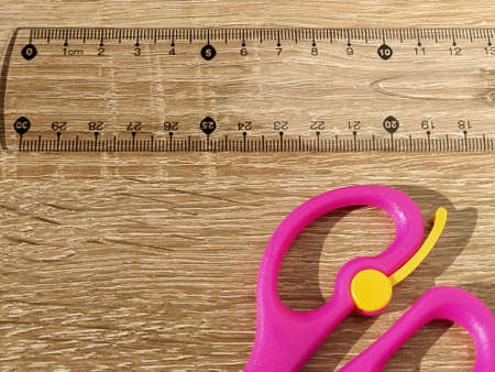 Transparent plastic school ruler on a wooden table. Millimeters and centimeters are marked in black. Measurement of length and width with a ruler. Bright pink scissors. Flat lay.の写真素材