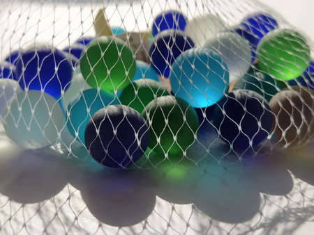 Multi-colored clickers or frosted glass balls for decoration. Blue, green, blue, beige balls in a mesh. Tactile toys for relaxation on a white background. The light shines through colored glass.の写真素材