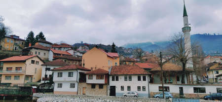 Sarajevo, Bosnia and Herzegovina - March 8, 2020: Sheher bridge over the Milatsk river. Spring. Turbid water in the river and bare trees. Turkish architecture and mosque. Mountains on the horizonのeditorial素材
