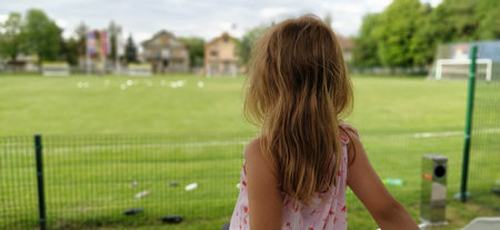 A girl sits with her back to the camera and watches a football match of childrens teams. Beautiful...