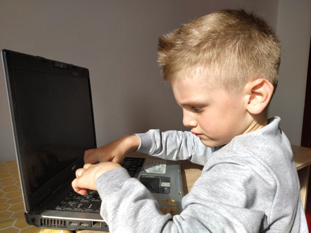 Sremska Mitrovica, Serbia, May 20, 2020 Blond boy with laptop. The child looks at the monitor and...