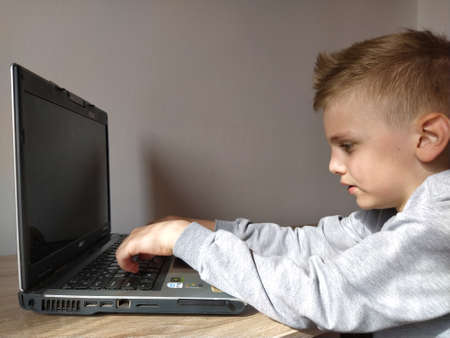 Sremska Mitrovica, Serbia, May 20, 2020 Blond boy with laptop. The child looks at the monitor and types on the keys.のeditorial素材