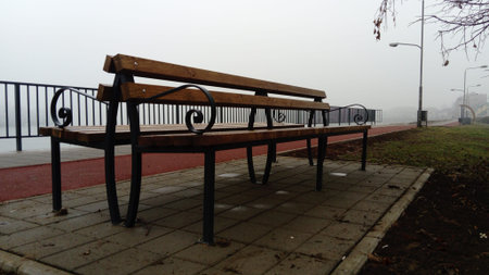 Wet bench on a foggy day. Metal curled wrought iron fence detail. Off-season melancholic mood.