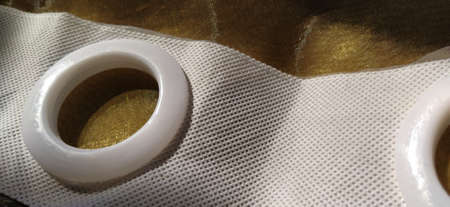 Plastic rings for attaching the fabric to the curtain rod. White plastic organza tulle eyelets. Light curtain in beige, brown or orange colors. White non-woven fabric. Finished textile edge. Interior elementの写真素材