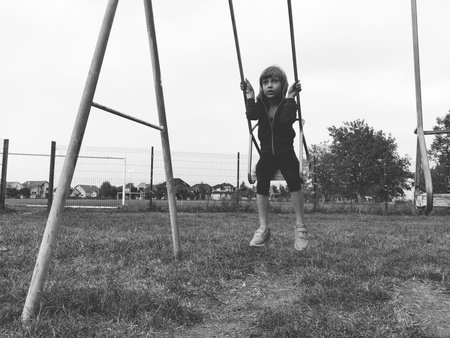 A 6-7 year old girl swinging on a swing against the background of a football field. Black and white...