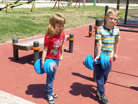 Sremska Mitrovica, Serbia. June 6, 2020. Flip-flops, weight lifting and weights, strength exercises. Two teenagers go in for sports on simulators, children on a sports ground.のeditorial素材