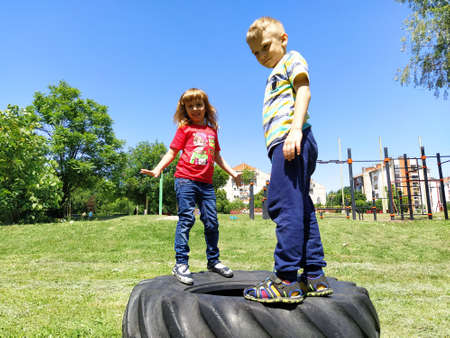 Sremska Mitrovica, Serbia, June 6, 2020. Children jump on the tire from the wheel. A boy and a girl stand on a rubber tire and try to rock it. Outdoor sports.のeditorial素材