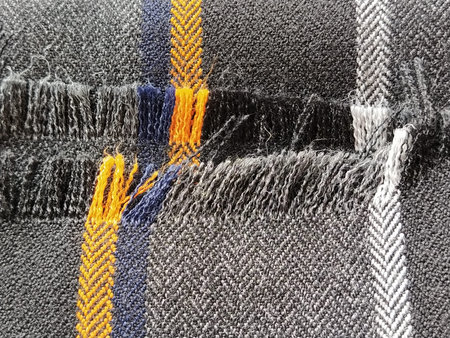 Light black-gray folded fabric with orange and dark blue stripes. Ripped, unfinished fabric edge....