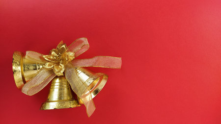 Christmas decorations. Gold bells with ribbon on red background.