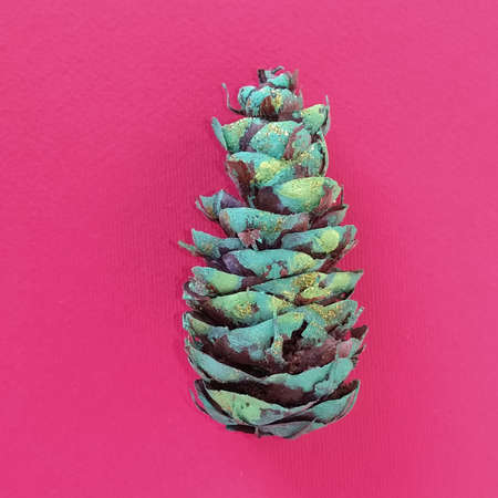 a beautiful pine cone colored green and decorated with gold sequins. In the background is a light blue fabric. Copy space. Christmas cone.の写真素材
