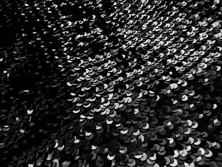 Sequin fabric. Black sequins with white and gray sheen. Reflection of light on individual elements in a chaotic manner. Sewing or Christmas decorative background.の写真素材