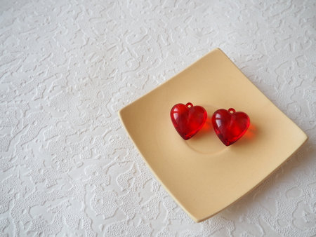 Valentine hearts. Red transparent plastic earrings on a white square plate and white. Greeting card with white background for the holiday valentine's day. An expression of love. Copy space.の写真素材