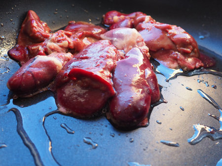 chicken liver, kidney and heart in a non-stick skillet. The offal of the bird is placed in a dark...