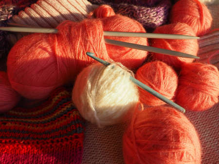 Tangles, snarls. Balls of yarn and thread, knitted clothes, knitting needles and crochet hooks. Pink, purple, red and white threads in skeins. Defocused image. Knitting and weaving as a hobbyの写真素材