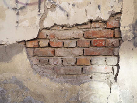the bricks are visible from under the plaster. Part of the cement coating has fallen off the old brick wall. Building renovation. Builders' mistakes. Temporary and weather influence.の写真素材