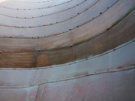 Metal surface with rivets and bolts. Abstract background of a military or industrial nature. Sheathing with dents, seams and nuts. Fasteners on metal. Steel or bronze panel.の写真素材