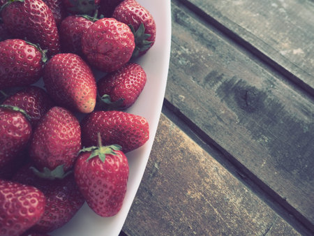Strawberries on a plate, wooden background. White dishes and delicious red large garden...