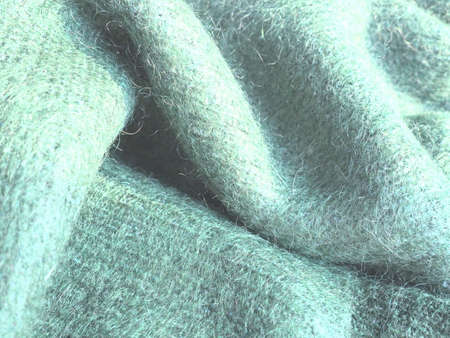 Knitted wool background. Warm winter clothes tied from green yarn brand Angora. A shaggy pile. A sample of knitting. Folded yarn.の写真素材