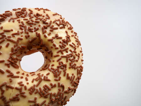 Donut close-up on white background. Delicious cake covered with vanilla icing and chocolate sprinkles. High-calorie breakfast or snack. Sweet dessert with vanilla and chocolate, donut or dough.の写真素材