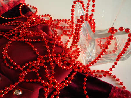 Red beautiful beads on bright scarlet velvet. Beautiful luxurious women's jewelry on soft fabric. Flat lay close-up. Women's stuff and cosmetics. Items as a background. Defocused soft focus.の写真素材
