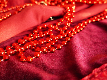 Red beautiful beads on bright scarlet velvet. Beautiful luxurious women's jewelry on soft fabric. Flat lay close-up. Women's stuff and cosmetics. Items as a background. Defocused soft focus.の写真素材