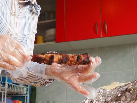 Grilled meat in disposable packaging and aluminum foil from the restaurant. Home delivery from restaurants and cafes. Female hands in disposable gloves hold meat on a stickの写真素材