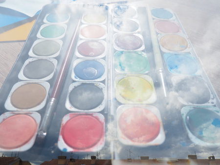 A set of watercolors of different colors for painting. Multi-colored round containers with bright paint. Tools for the lesson of drawing. Double composition. Clouds and sky. Painted clouds. Collage.の写真素材