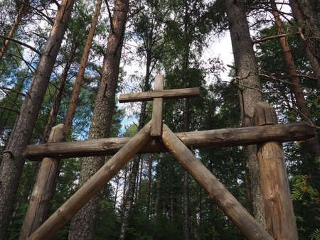 Entrance to the cemetery. Towering cross. Wooden gate with a cross to the Christian Orthodox rural cemetery, Orzega village, Karelia, Russia. Pine forest. Sky with clouds. Religious or Halloween themeの写真素材