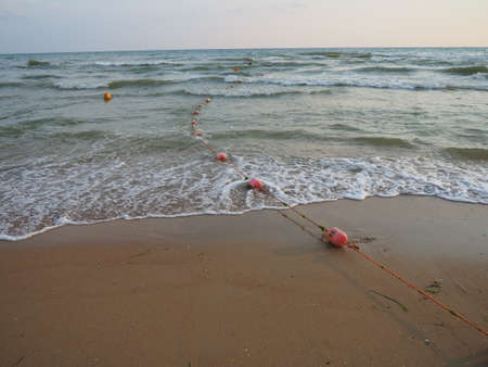 Buoys on a rope near sea water. The buoys are pink restraints to alert people to the depth of the water. Rescue of the drowning. Delimiting a place on a sandy beach between hotels. Wave with bubblesの写真素材