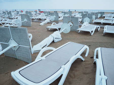 A beach umbrella lay folded on a sandy beach after bad weather. Storm at sea. End of the beach season due to typhoon and cyclone. Loungers, umbrellas and hotel furniture. Wind-upturned structuresの写真素材