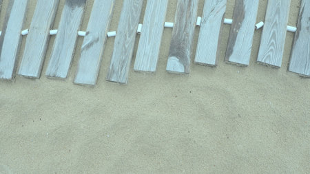Wooden footbridge on a sandy beach. Uneven, damp wooden planks held together. The edge of the beach season at the hotel. No people, copy space. Equipped sandy beach after a storm or cyclone. Tourismの写真素材
