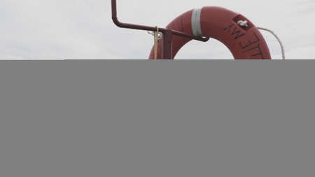 Lifebuoy on a sandy beach. Orange circle on a pole to rescue people drowning in the sea. Rescue point on the shore. Sky and sea in the background.の写真素材