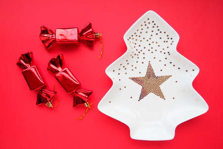 Christmas tree with gold ornaments and a star in the middle. Red background. Candy in a red shiny wrapper. Background for advertisements and inscriptions. Gift preparation. Christmas decorationsの写真素材