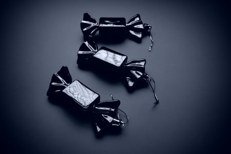 Christmas decorations in the form of sweets. Three candies in wrappers on a dark background. Beautiful decorations for New Years and Christmas. Hanging threads. Blue and black background with vignetteの写真素材