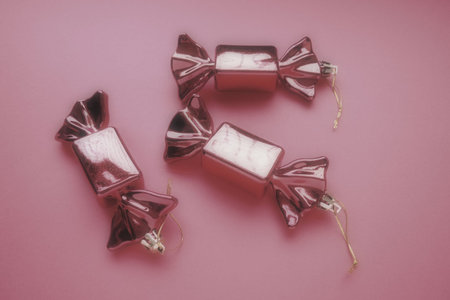 Christmas decorations in the form of sweets. Three candies in wrappers on a peaceful pink...