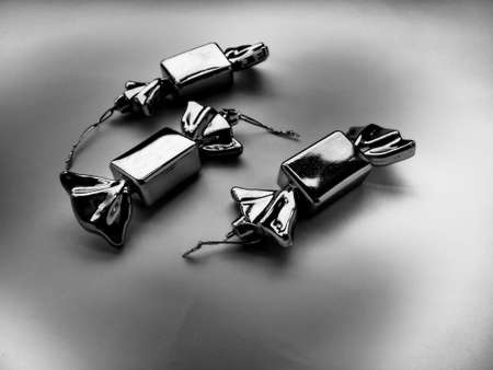 Christmas decorations in the form of sweets. Three candies in wrappers on a gray background. Beautiful decorations for New Years and Christmas. Hanging thread. White and black background with vignetteの写真素材