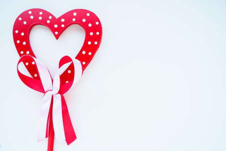 Valentine's day concept. Red wooden heart with white dots and ribbon bow on a stick. White background. A beautiful bow as a decoration. Love and relationships. Recognition or congratulations.の写真素材