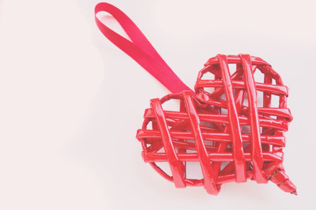 Red braided heart with a silk ribbon on a pink background. Valentine's Day. copyspace. A nice souvenir - a pendant at an angleの写真素材
