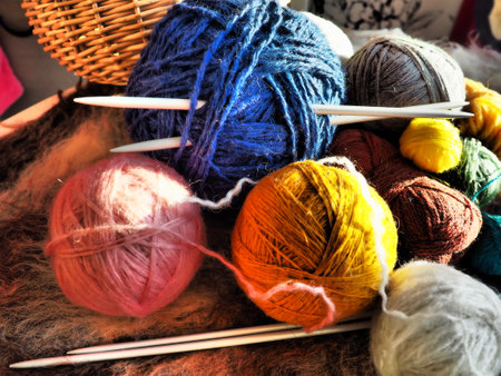 Knitting a scarf or sweater from gray, blue, white and orange yarns. Hanks of woolen and acrylic threads. Knitting as a hobby. Accessories, knitting needles, crochet hooks.の写真素材