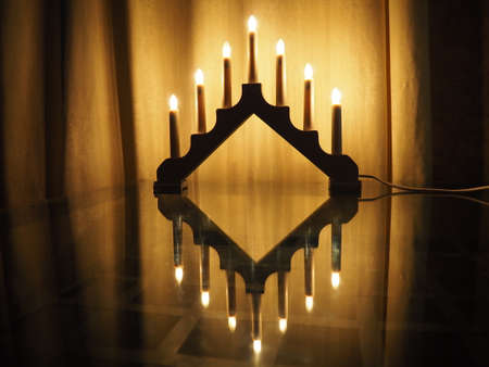 Schwibbogen arch luminaire, a triangular candlestick on glass table. Yellow background. Evening, romantic, festive, religious or mystical atmosphere. Burning light bulbs that resemble candlelightの写真素材