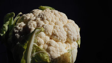 Cauliflower close-up on a black background. Side lighting. Fresh head of cabbage. Green vegetables....