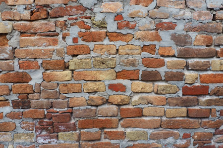 Brick wall of an ancient fortress. Uneven red and brown bricks with cement. Brick background