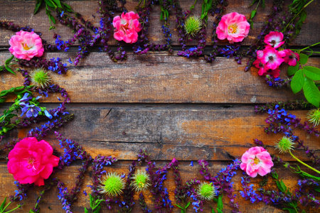 Flowers in a circle on a wooden background. Postcard for the holiday. Roses, geraniums, lavender, sage and hairy chestnuts are placed along the edges on dark boards. Background copy space, flat layの写真素材