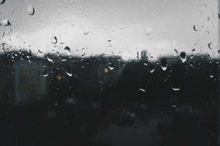 bad weather in the city. Buildings, houses, cars outside the window. Cloudiness cumulus clouds. meteorology and weather forecast. Raindrops run down the glass. Storm and Storm and wind on city streetsの写真素材