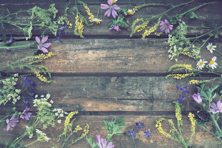Multicolored wildflowers are arranged in a circle on a wooden table background. Chamomile, sweet...