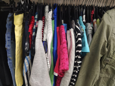 Clothes hung on hangers. Assortment of second hand store. Childrens and womens shirts, blouses, sweaters hanging on a rack, ready for sale to customers. Saving money in crisis. Cheap shopping.の写真素材