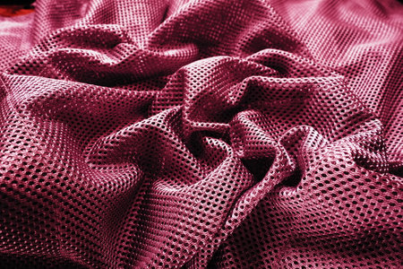 Synthetic fabric with holes, laid in waves and twisted into folds. Beautiful drape. Fabric for curtains, interior design, and decor. Twisted or wrinkled red burgundy porous fabric.の写真素材