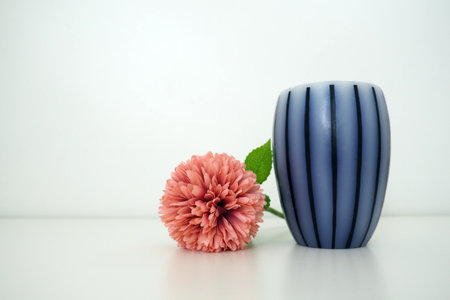 Scented gray striped candle on a white surface. Pink terry artificial flower on a white background. Still life, interior decoration option. Room decor. Free space for textの写真素材