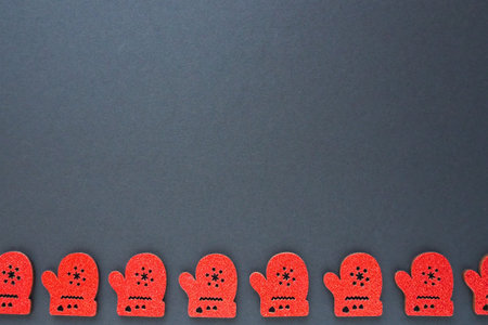 New Year and Christmas decorations in the form of red cardboard mittens with sparkles. The mittens are lined up along the bottom edge of the black paper. Christmas background. Copy space.の写真素材