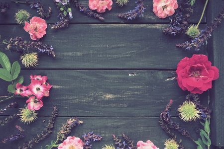 Flowers in a circle on a wooden background. Postcard for the holiday. Roses, geraniums, lavender, sage and hairy chestnuts are placed along the edges on dark boards. Background copy space, flat layの写真素材